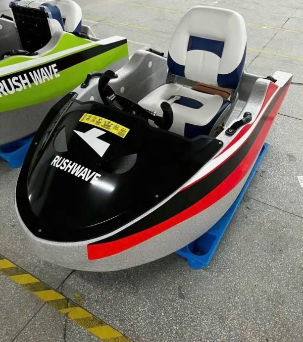 Rush Wave 2025 15 kW Electric Go-Kart Boat, angled factory view Rush Wave 2025 15 kW Electric Go-Kart Boat with a white hull, red-and-black side stripes, black RUSHWAVE windshield, and white-and-blue seat in a factory.