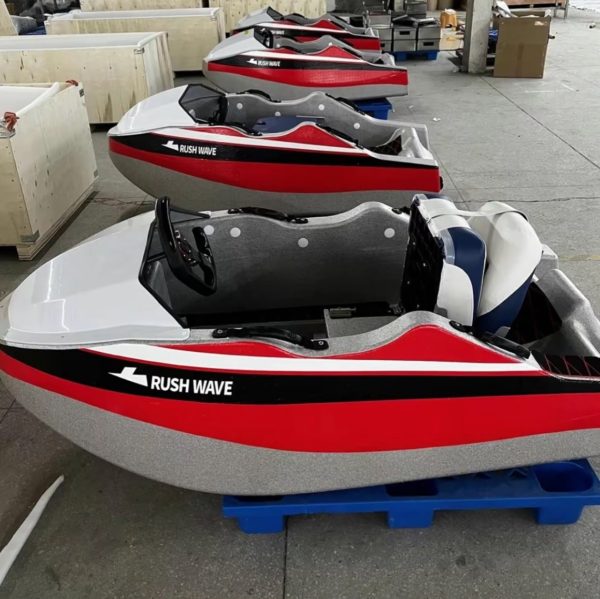 Rush Wave 2025 15 kW Electric Go-Kart Boat, side lineup factory view Rush Wave 2025 15 kW Electric Go-Kart Boat with a silver-white hull, red-and-black side stripes, white-and-blue seat, steering wheel with red display, and RUSHWAVE branding in a factory lineup.