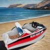 Rush Wave 2025 15 kW Electric Go-Kart Boat, beach scene Rush Wave 2025 15 kW Electric Go-Kart Boat with a white hull, red-and-black side stripes, RUSHWAVE branding, white-and-blue seat, wood-look rear deck, steering wheel with red display, and rear jet outlet beside the sea.