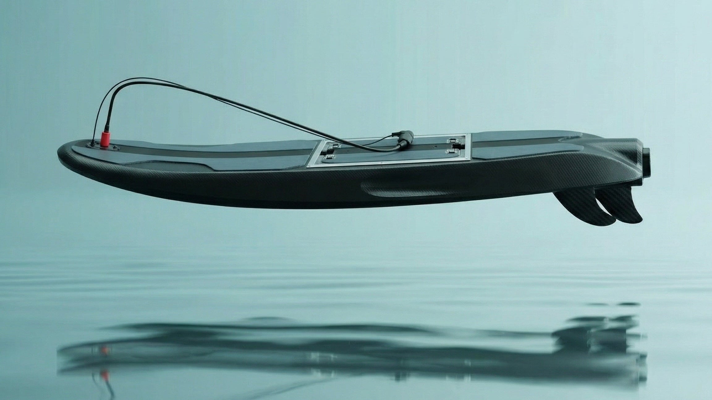Side view of the dark Rider Plus G3 surfboard with a leash and three fins.